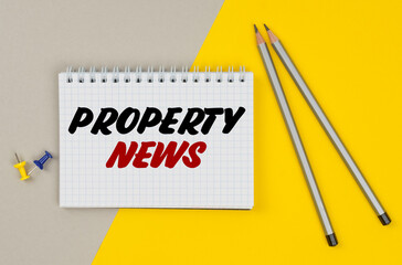 On a yellow-gray background are pencils, buttons and a notebook in which it is written - PROPERTY NEWS