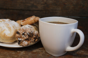 A plate with chocolate chip cookies and a cup of hot coffee on an old wooden table. White cup.