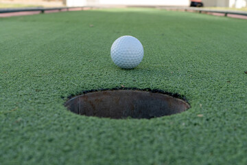 Miniature or mini golf hole close up with ball in center on green artificial turf outdoors.