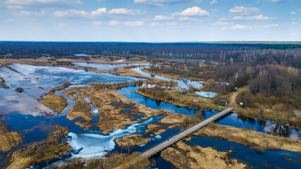 Aerial landscape view on river with flooded meadows and beautiful fields.. Wooden bridge over small river in spring. Travel concept.