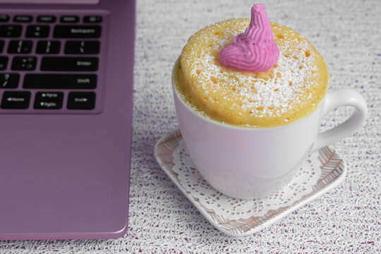 pink laptop. A cupcake in a mug is on a saucer. The concept of a quick snack for lunch. Microwave Vanilla Cupcake. High quality photo