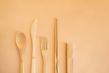 Eco friendly bamboo cutlery set on a beige background top view. Zero waste concept. Spoon, fork, knife, toothbrush, tube and chinese sticks.