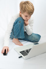 A child of the European type is sitting barefoot in front of a laptop. The blond looks attentively at the monitor. Cozy home environment. Home schooling concept. Enthusiastic computer game
