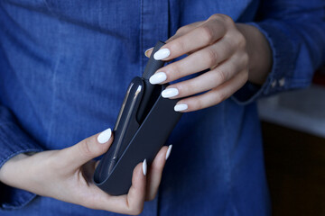 female hand with white polish taking electronic cigarette