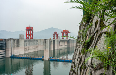 Three Gorges Dam, China - May 6, 2010: Yangtze River. Green foliage on gray rock up front with dam...