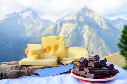 Tasty Swiss cheeses and dark pure chocolate, emmental, gruyere, appenzeller served outdoor with Alpine mountains peaks on background