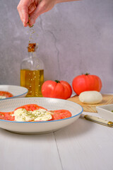 Seasoning with oregano a tasty salad of ripe tomatoes and mozzarella cheese