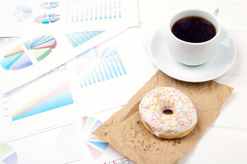 Desk - business documents, graphics, donuts and a cup of coffee. Breakfast in the office. Top view.