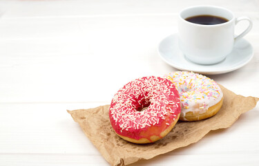 Two donuts and cup of coffee on a light wooden background.