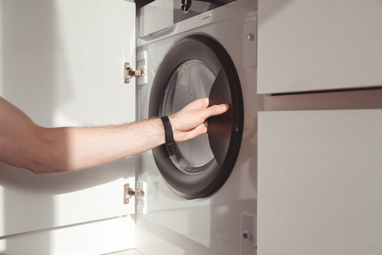 man's hand opening built-in washing machine in kitchen