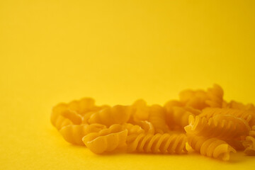 Pasta in the form of spirals and shells on a yellow background.