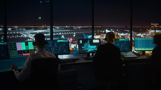 Diverse Air Traffic Control Team Working in Modern Airport Tower at Night. Office Room Full of Desktop Computer Displays with Navigation Screens, Airplane Departure and Arrival Data for Controllers.