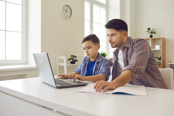 Caucasian father help son with online homework. Parent and schoolchild sitting at desk front of...