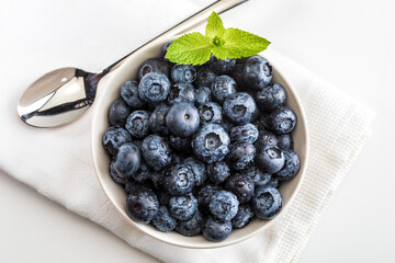 Fresh and raw blueberries with drops of water. In bowl on white napkin with spoon and ready to eat. Top view with copy space.
