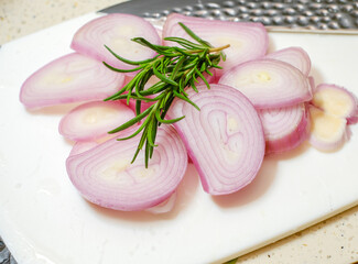 Fresh cut onion in a white cutting board sliced fresh with rosemary on top.
