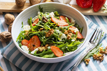 Vegetarian and healthy salad of green, natural, raw and freshly cut arugula (rúgula) sprouts and leaves (brassicaceae), fresh strawberries, walnuts, goat cheese, olive oil. Mediterranean diet food. 