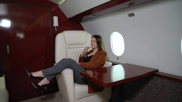 Woman passenger in airplane business first class with champagne. Luxury girl in private jet flight travel. High quality 4k footage