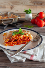 Lasagna with balanese sauce and basil served on a platter next to a baking dish on a light wooden background