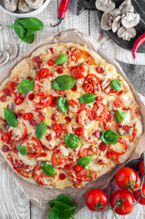 Pepperoni pizza with tomatoes, mushrooms, mozzarella, parmesan and basil on a light gray background. Top view
