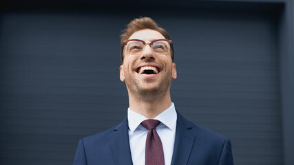 positive businessman in formal wear and glasses laughing while looking up.