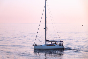 Sailing yacht in the blue sea during beautiful pink sunset.