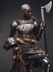 Wild barbaric person with black skin wielding an axe posing in dark background
