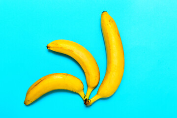 Top view. Three yellow bananas on a blue background.