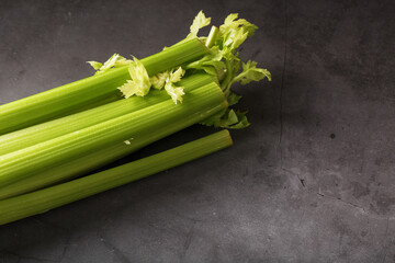 Fresh celery stalks on a black textured background.