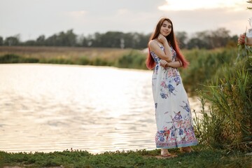 Fototapeta na wymiar beautiful redhead girl in white dress in summer by the pond