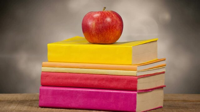 Animation of stack of books with red apple on top over glowing lights