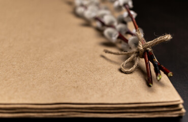 Defocused stack of brown craft paper and willow twigs with linen rope bow. Spring concept in dark style and colors. Banner with copy space.
