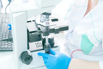 laboratory assistant in blue gloves works with a microscope