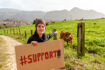 vegan animal rights activist poses with a support sign in front of livestock. young girl asking for...