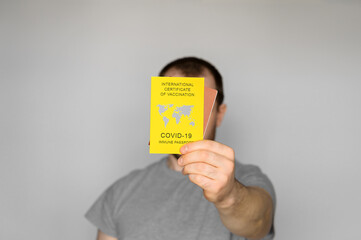 Adult man wearing t-shirt holding yellow International Certificate of Vaccination on gray...