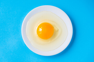 Raw egg on a white plate. View from above. Fresh egg with a bright yolk on a blue background.