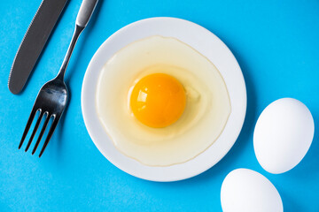 Raw egg on a white plate. View from above. Fresh egg with a bright yolk on a blue background.