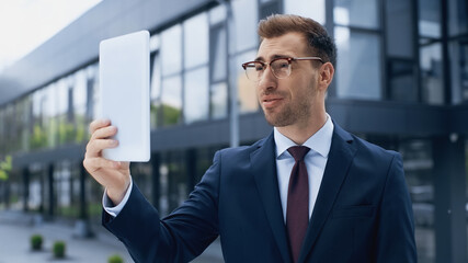 businessman in glasses holding digital tablet outside.