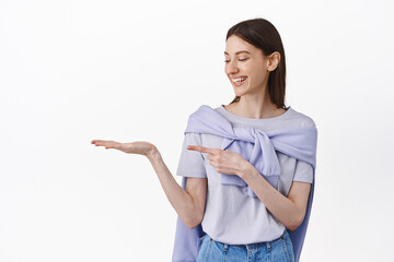 Let me introduce you this. Pretty young woman looking at her open hand holding logo product,...