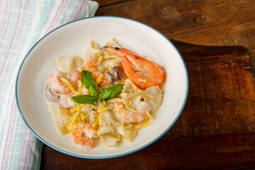 Pasta with shrimps in a creamy sauce on a gray plate on a wooden table on a napkin.
