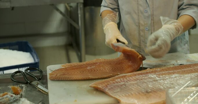 Close-up shot of a woman worker's hand in a market factory, a woman stands on the process of cutting a salmon and stacking red fish fillets. Fish meat processing plant. Fish factory, fish cutting
