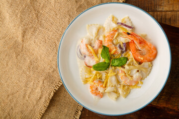 Farfalle pasta with shrimps in a creamy sauce on a gray plate on a wooden table on a linen napkin.