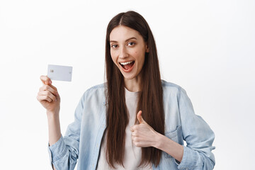 Fototapeta premium Image of female student say yes, showing credit card and thumb up, approve and recommend bank, easy contactless payment, standing over white background