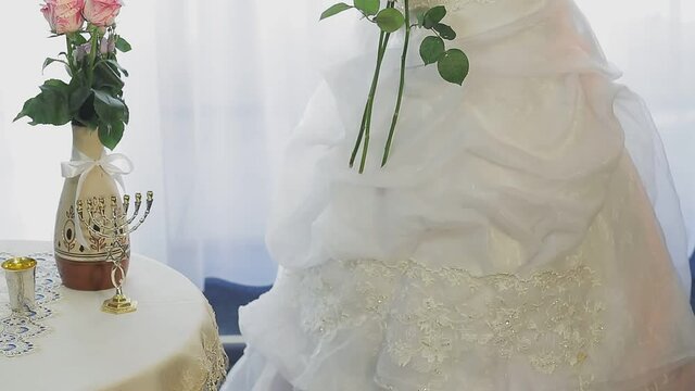 Jewish bride in a wedding dress and veil wearing a medical mask in the synagogue hall before the chupa ceremony with a bouquet of flowers. Bottom up panorama