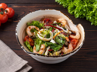 Fresh Mediterranean salad with seafood. Salad with shrimps, squid and herbs on a wooden background. Space for the text. Menu, restaurant, cafe. Rustic style. Copy space. Dietary nutrition.