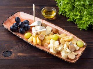 Cheese dish with various cheeses, grapes, nuts, honey on a rustic wooden background. Wine appetizer for guests. Assorted cheese. Space for the text. Menu, restaurant, cafe. Rustic style. Copy space.