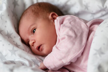 A newborn baby lies in a blanket for two weeks. Girl in a pink sweater. Motherhood and care. Close-up.