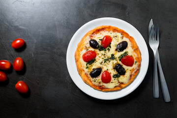 Overhead view of pizza with space for text. Fresh cherry tomato a side. Black stone texture background.