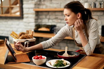 Young woman looking for recipe on digital tablet while making breakfast at home. - obrazy, fototapety, plakaty