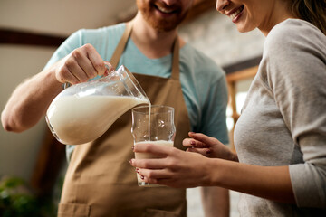 Close-up of man pouring milk into girlfriend's glass for breakfast in the morning.