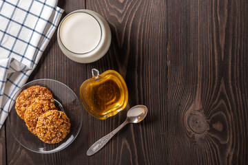 glass of milk, oatmeal cookies and honey on a dark wooden table top view